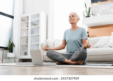 Mature fit athlete meditating in lotus position while watching online training tutorial on laptop. Home training workout concept. Social distancing - Powered by Shutterstock