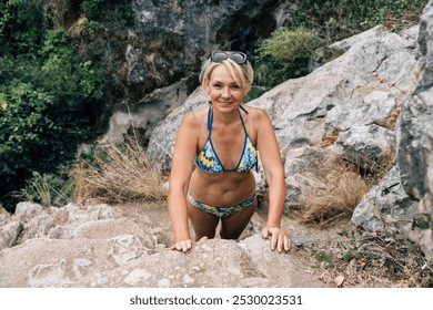 A mature, fit woman in a colorful bikini looking up while navigating a rocky terrain near Cueva del Gato in Ronda, enjoying an adventurous hike - Powered by Shutterstock