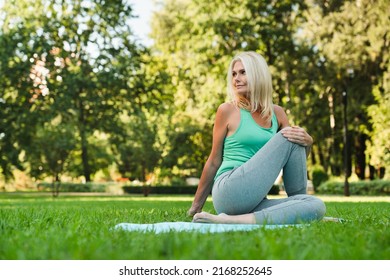 Mature fit woman stretching her body on fitness mat, doing workout in park, practicing breathing exercises. Active healthy lifestyle. - Powered by Shutterstock