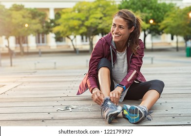 Mature fitness woman tie shoelaces road  Cheerful runner sitting floor city streets and mobile   earphones wearing sport shoes  Active latin woman tying shoe lace before running 