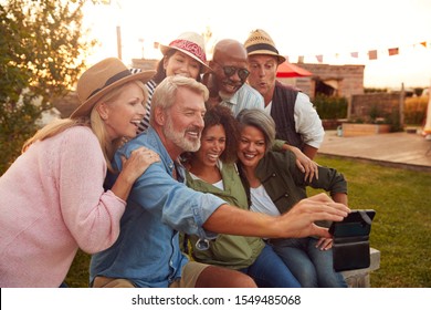 Mature Friends Sitting Around Fire At Outdoor Campsite Taking Selfie