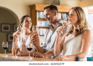 Mature Friends Tasting Red And White Wine At Vineyard. Senior Couple And Visitor Drinking White Wine. Customers At A Bar Winetasting And Talking To Each Other.
