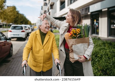 Mature granddaughter carrying grandmother's shopping bag. Senior woman and caregiver going to home with groceries from supermarket, during cold autumn day. - Powered by Shutterstock