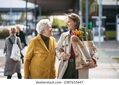 Mature granddaughter carrying groceries out to her grandmother's car. Senior woman shopping at the shopping center, needing help loading groceries into car. - Powered by Shutterstock