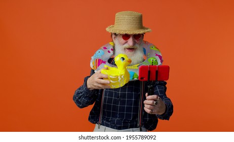 Mature Grandfather Traveler Blogger With Swimming Ring And Inflatable Duck Toy, Taking Selfie On Mobile Phone, Make Video Call Online. Studio Shot. Senior Man On Summer Holiday Vacation, Trip. Tourism