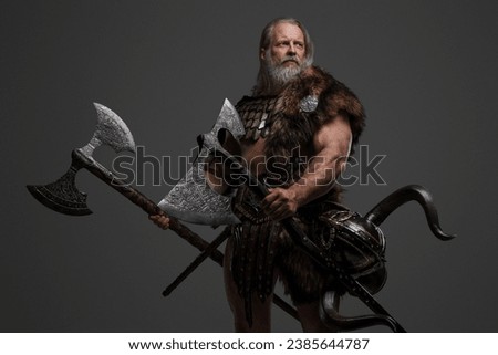 Mature gray-haired bearded Viking warrior in fur and light armor, wielding two enormous axes against a neutral background