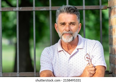 Mature Grey Bearded Male With Crossed Arms. Senior Man Smiling Outdoor. Wise Thoughts About Life. Live And Learn. Portrait Of A Proud Mature Man Standing With Folded Arms With Park In Background.