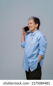 Mature Grey Hair Woman Talking On The Phone Turn Sideways Holding Smartphone In Her Hand Wearing Blue Shirt And Black Skirt. Pretty Woman In Blue Shirt Isolated On White Background.