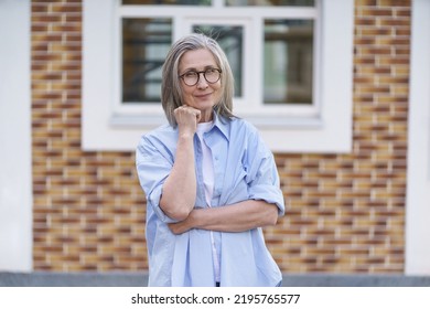 Mature Grey Hair Woman Wearing Glasses Standing Outdoor Traveling Around World At Retirement. Senior Woman Meeting Her Family. Mature Woman With Perfect Skin Wearing Blue Shirt Standing Outside. 