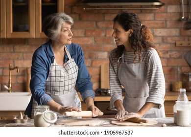 Mature grey haired woman with grownup daughter chatting, cooking homemade pastry, rolling dough, standing in kitchen at home, family spending leisure time together, preparing pie or bread together - Powered by Shutterstock