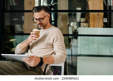 Mature grey man drinking coffee while working with tablet computer in office - Powered by Shutterstock