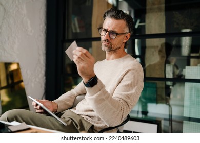 Mature grey man examining samples while working with tablet computer in office - Shutterstock ID 2240489603