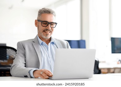 Mature handsome grey-haired businessman in a smart blazer working diligently on his laptop, reflecting the focus and engagement that characterize today's business leaders - Powered by Shutterstock