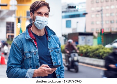 A Mature Handsome Man With A Beard Chats On His Phone And Wears A Face Pollution Mask To Protect Himself From Coronavirus.