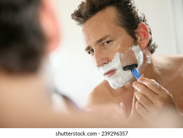 Mature handsome man shaving in front of mirror