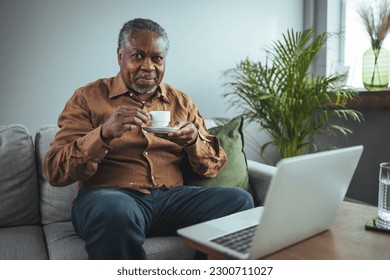 Mature handsome man sitting on the sofa drinking coffee. A senior black man enjoys a cup of coffee at home. Elderly man at home drinking coffee  - Powered by Shutterstock