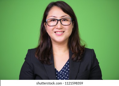 Mature happy beautiful Asian businesswoman smiling with eyeglasses against green background - Powered by Shutterstock