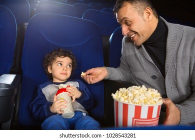 Mature Happy Handsome Hispanic Man Offering His Adorable Little Son Popcorn While Sitting At The Movie Theatre Together Copyspace Father Kids Children Entertainment Food Snack Meal Parenting Leisure