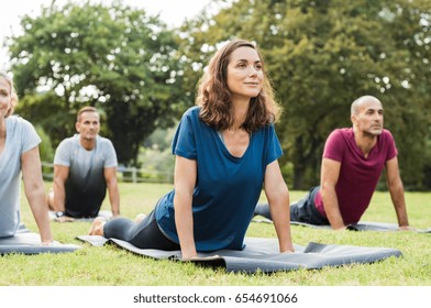 Mature healthy people doing yoga at park. Group of multiethnic people exercising on green grass with yoga mat. Happy men and smiling women in yoga class doing exercise outdoor.