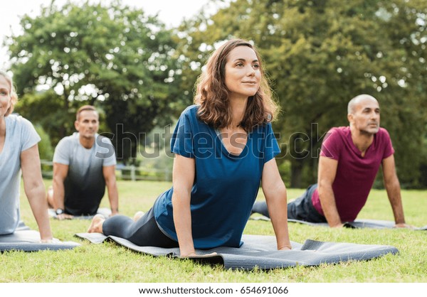 Mature\
healthy people doing yoga at park. Group of multiethnic people\
exercising on green grass with yoga mat. Happy men and smiling\
women in yoga class doing exercise\
outdoor.\

