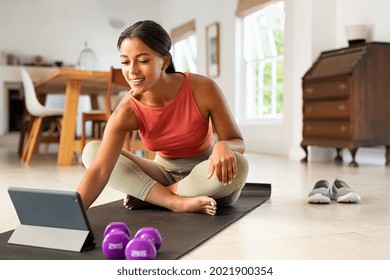 Mature healthy woman using app on digital tablet at home to train in hata yoga. Happy smiling indian lady watching exercise tutorials on digital tablet while working out with dumbbells at home. - Powered by Shutterstock