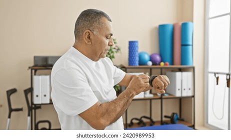 Mature hispanic man checking smartwatch in rehab clinic room with exercise equipment. - Powered by Shutterstock