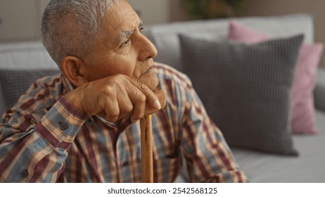 A mature hispanic man with grey hair and a patterned shirt rests on a wooden cane in a cozy living room. - Powered by Shutterstock