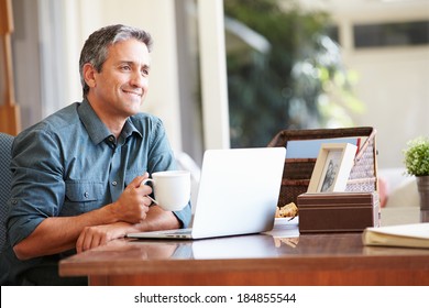 Mature Hispanic Man Using Laptop On Desk At Home