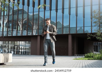 Mature hispanic senior business man in casual clothes using smartphone cellphone app walking at office building. Full body of Latin middle age freelance businessman holding mobile cell phone outdoors - Powered by Shutterstock - Get 15% off with code: PIKWIZARD15