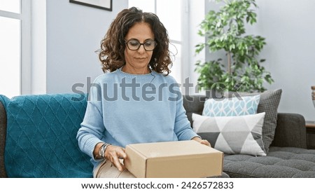 Mature hispanic woman with curly hair unpacking a box in her cozy modern living room.
