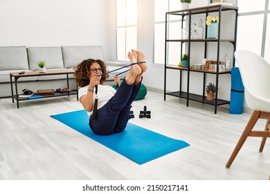 Mature hispanic woman doing exercise with elastic bands at the living room at home - Powered by Shutterstock