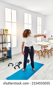 Mature Hispanic Woman Doing Exercise Lifting Dumbbells At The Living Room At Home