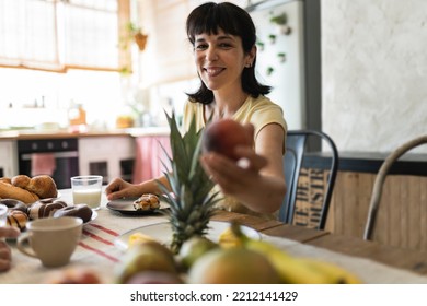 Mature Hispanic Woman Eating Breakfast Picks Fruit From Lunch Table,