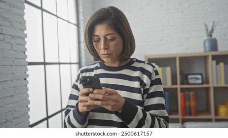 Mature hispanic woman focused on smartphone in bright, cozy living room. - Powered by Shutterstock