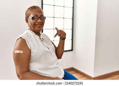 Mature Hispanic Woman Getting Vaccine Showing Arm With Band Aid Looking Confident With Smile On Face, Pointing Oneself With Fingers Proud And Happy. 