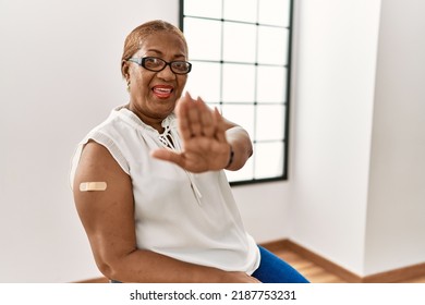 Mature Hispanic Woman Getting Vaccine Showing Arm With Band Aid Doing Stop Gesture With Hands Palms, Angry And Frustration Expression 