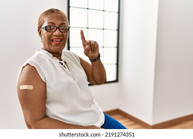 Mature Hispanic Woman Getting Vaccine Showing Arm With Band Aid Smiling Amazed And Surprised And Pointing Up With Fingers And Raised Arms. 