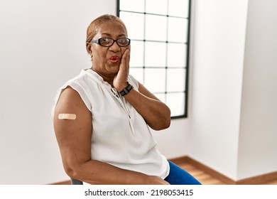 Mature Hispanic Woman Getting Vaccine Showing Arm With Band Aid Afraid And Shocked, Surprise And Amazed Expression With Hands On Face 