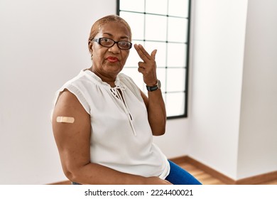 Mature Hispanic Woman Getting Vaccine Showing Arm With Band Aid Shooting And Killing Oneself Pointing Hand And Fingers To Head Like Gun, Suicide Gesture. 