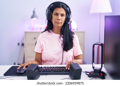 Mature Hispanic Woman Playing Video Games At Home Relaxed With Serious Expression On Face. Simple And Natural Looking At The Camera. 