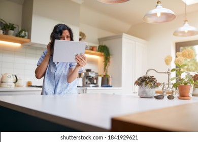 Mature Hispanic Woman In Pyjamas At Home In Kitchen Checks Hair And Appearance With Digital Tablet - Shutterstock ID 1841929621