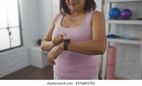 A mature, hispanic woman with short hair at a gym checks her fitness watch in an indoor setting. - Powered by Shutterstock