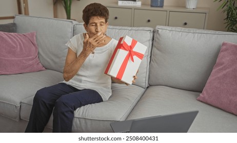 Mature hispanic woman with short hair making a video call from her living room, holding a gift box with a red ribbon and blowing a kiss. - Powered by Shutterstock