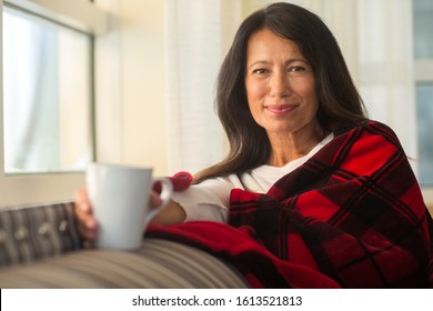 Mature Hispanic Woman Sitting On The Sofa Sitting On A Sofa Drinking Coffee.