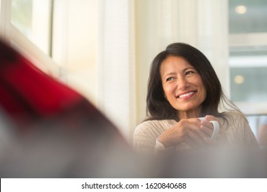 Mature Hispanic Woman Sitting On The Sofa Drinking Coffee.