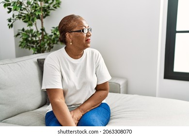 Mature Hispanic Woman Sitting On The Sofa At Home Looking To Side, Relax Profile Pose With Natural Face With Confident Smile. 