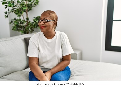 Mature Hispanic Woman Sitting On The Sofa At Home Looking Away To Side With Smile On Face, Natural Expression. Laughing Confident. 