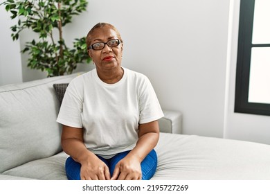 Mature Hispanic Woman Sitting On The Sofa At Home Relaxed With Serious Expression On Face. Simple And Natural Looking At The Camera. 