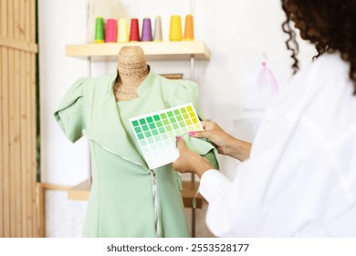 A mature Hispanic woman, skilled in sewing and design, reviews a color palette while working on a stylish green dress in her creative studio. Her focus showcases her artistic process. - Powered by Shutterstock