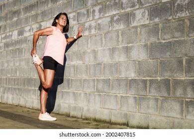 Mature hispanic woman with sportswear stretching on a wall